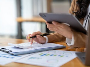 Frau am Schreibtisch mit Unterlagen und Taschenrechner, Auswertung von Daten