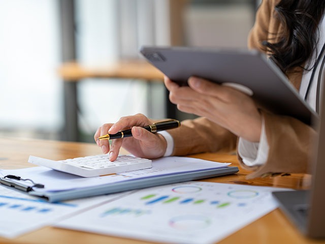 Frau am Schreibtisch mit Unterlagen und Taschenrechner, Auswertung von Daten