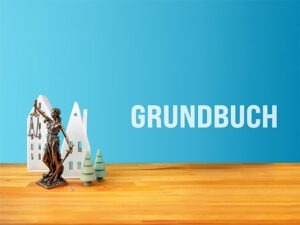 Modellhäuser, die Justizia und der Schriftzug Grundbuch auf blauem Hintergrund