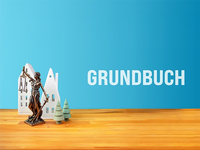 Modellhäuser, die Justizia und der Schriftzug Grundbuch auf blauem Hintergrund